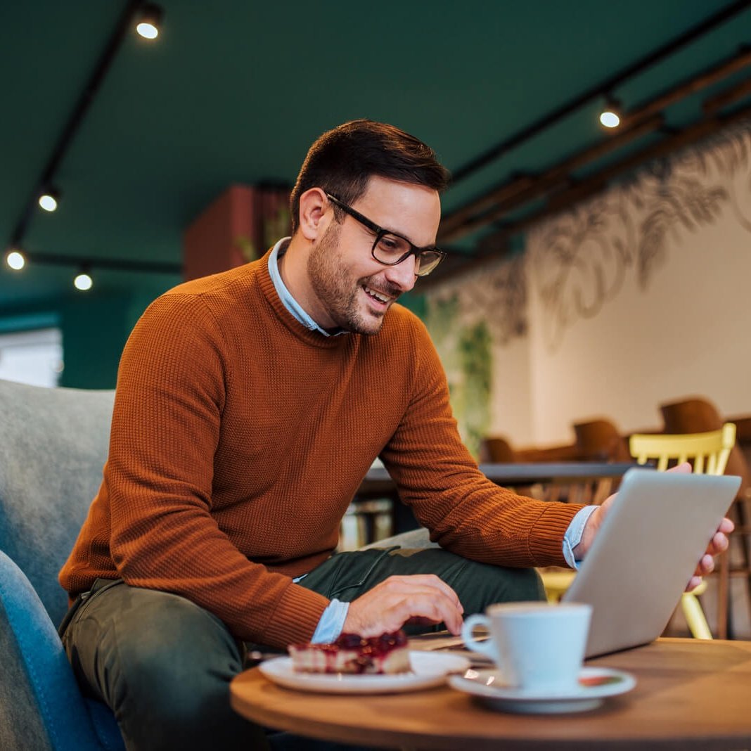 Cheerful Man Using Laptop In A Cozy Restaurant Po 2024 10 18 07 51 26 Utc 1 1 Cropped
