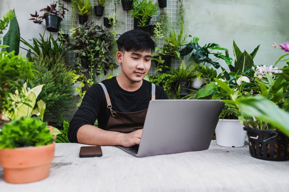 Young Gardener Man Use Smartphone And Laptop Onlin Y86ANRP